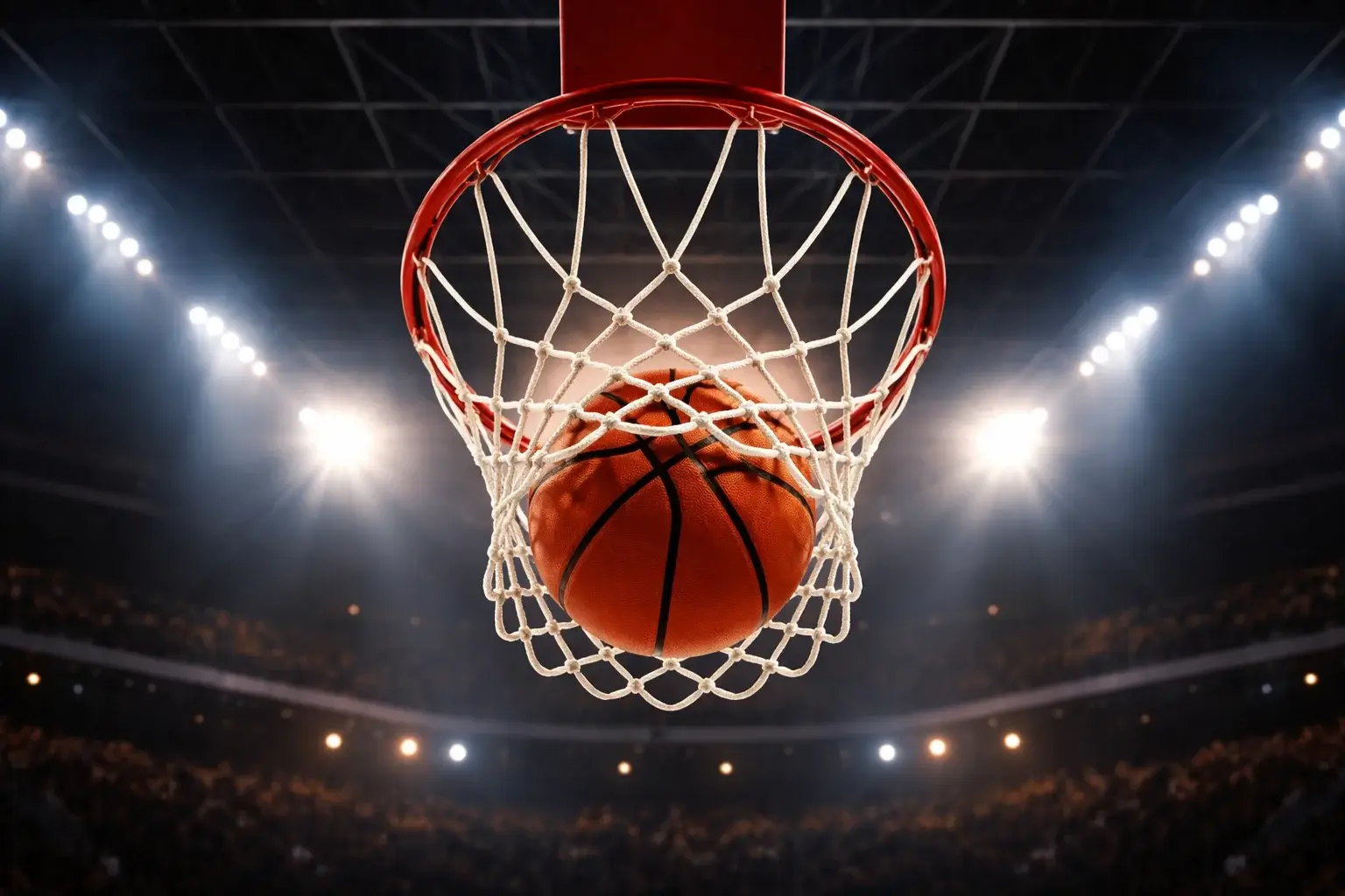 Palla da basket che entra nel canestro vista dal basso con luci del palazzetto
